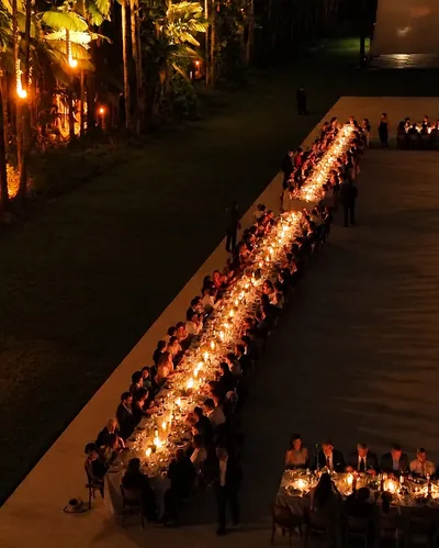 A mesa longa do jantar, acesa a velas, entre as palmeiras