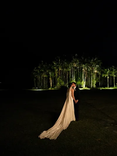 A noiva, com o vestido estendido no gramado, diante das palmeiras iluminadas à noite