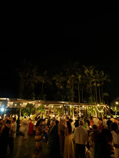 A festa vista de fora, com a tenda iluminada entre as palmeiras