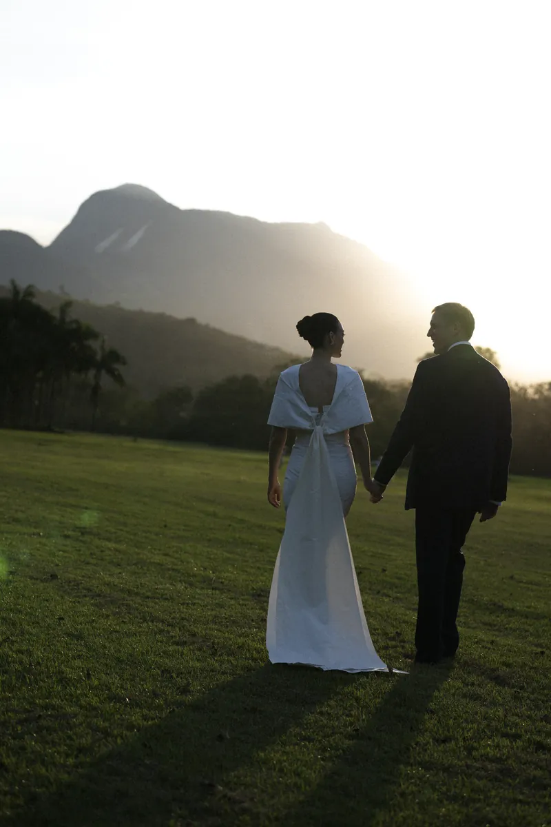 Os noivos de mãos dadas no gramado, diante da Serra do Mar, no fim da tarde